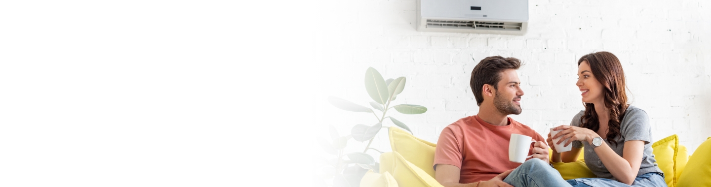 Couple sitting on a couch underneath a ductless heat pump unit