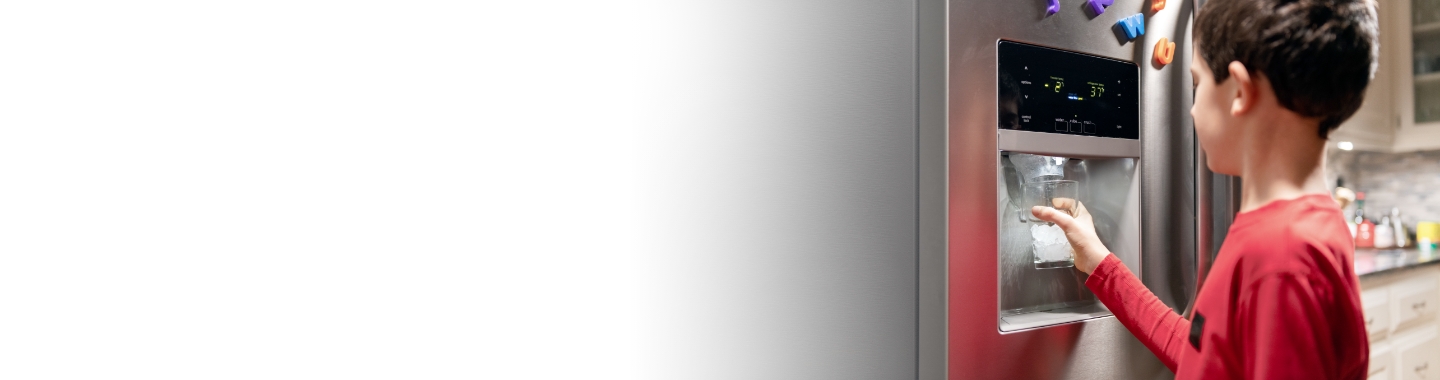 Young boy filling his water glass at the refrigerator 