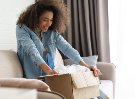 Woman sitting on couch smiling while opening shipping box